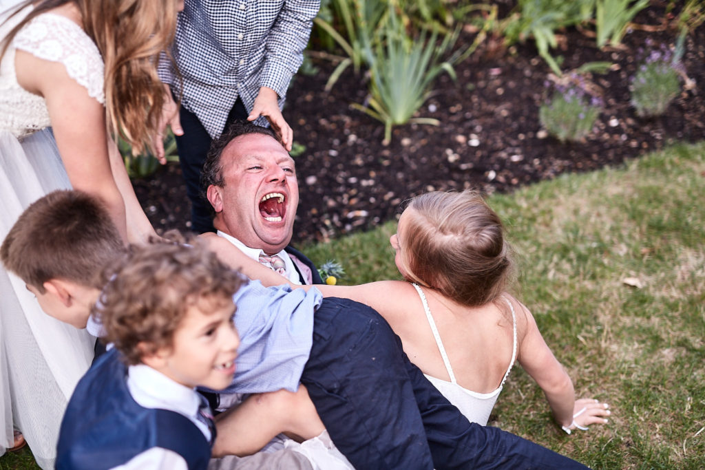 Man laughing as children pile on top of him on the lawn