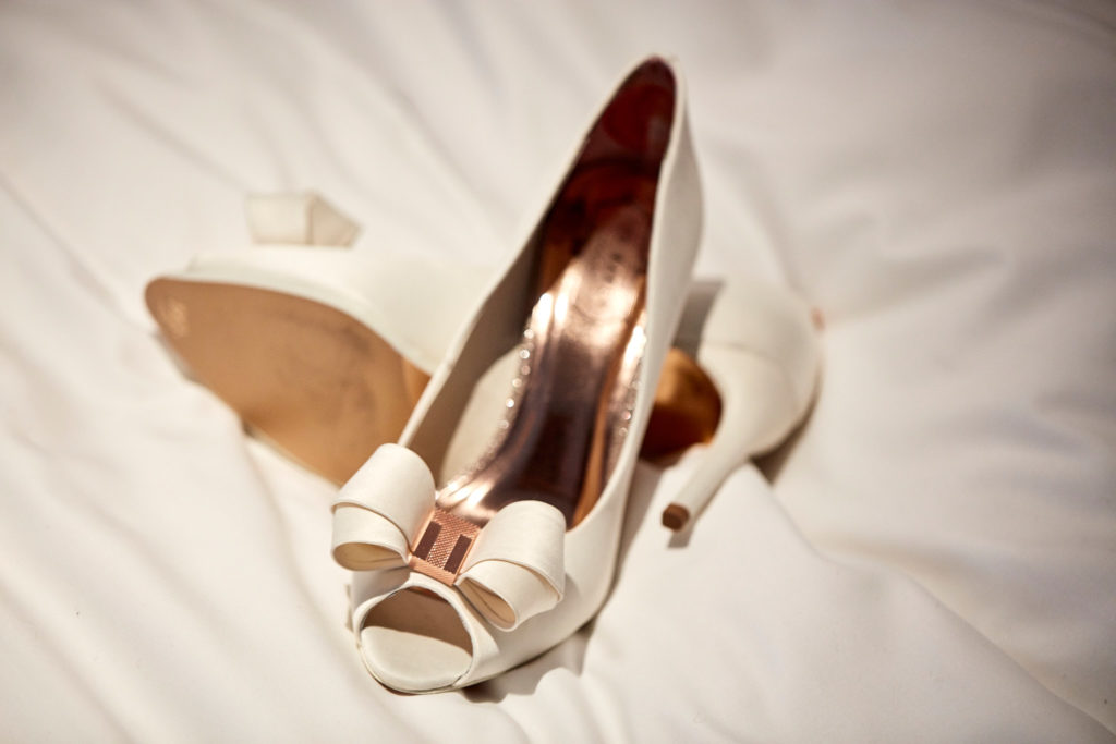 Ivory peep-toe bridal shoes with bows on a white bed
