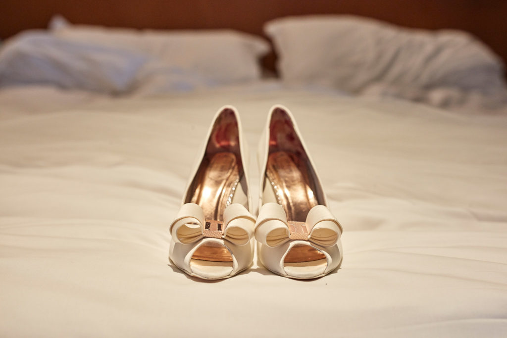 Ivory bridal shoes on a hotel bed