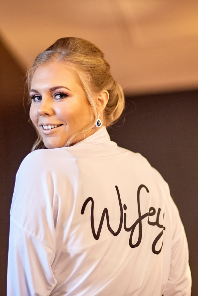 Bride looking over her shoulder in a white robe with "Wifey" on the back