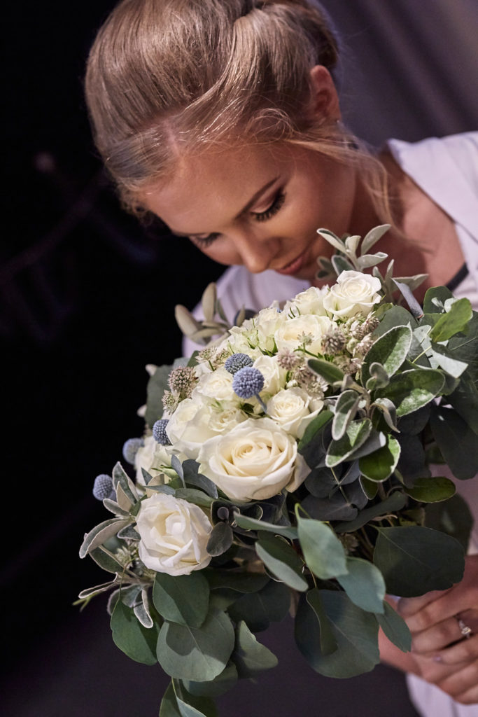 Bride looking down at her bouquet of white roses and eucalyptus