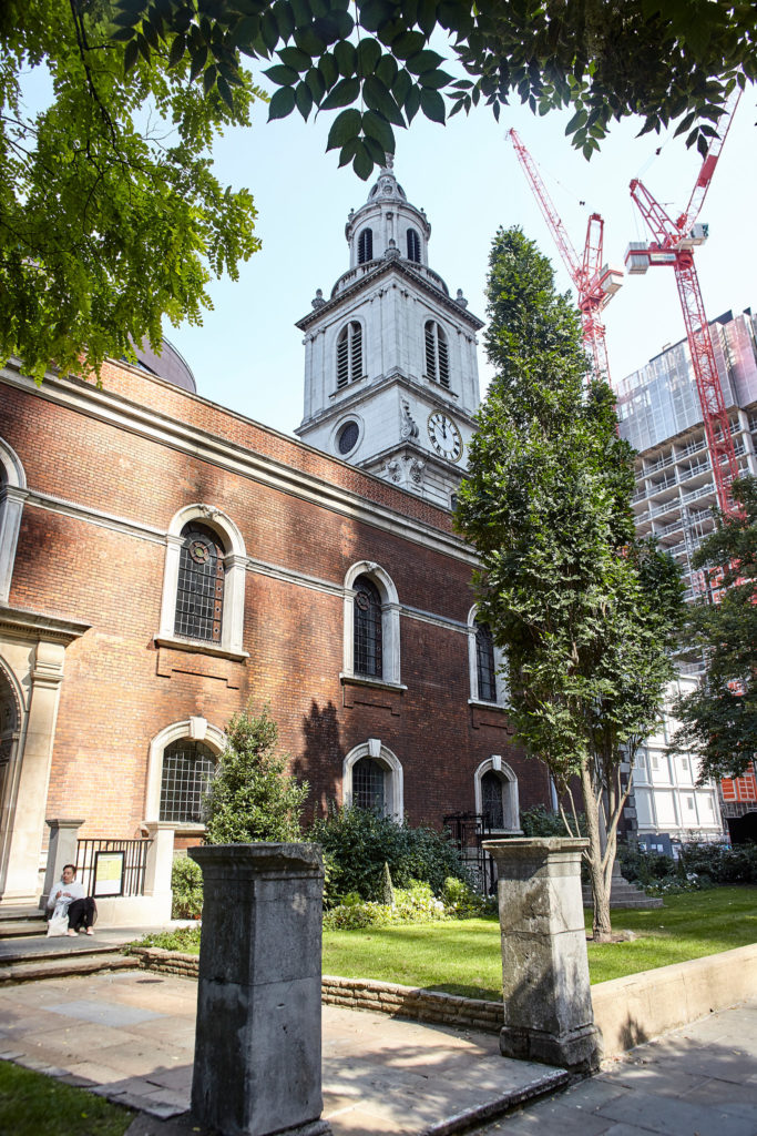 Red-brick London church with a white tower, with cranes on the skyline behind
