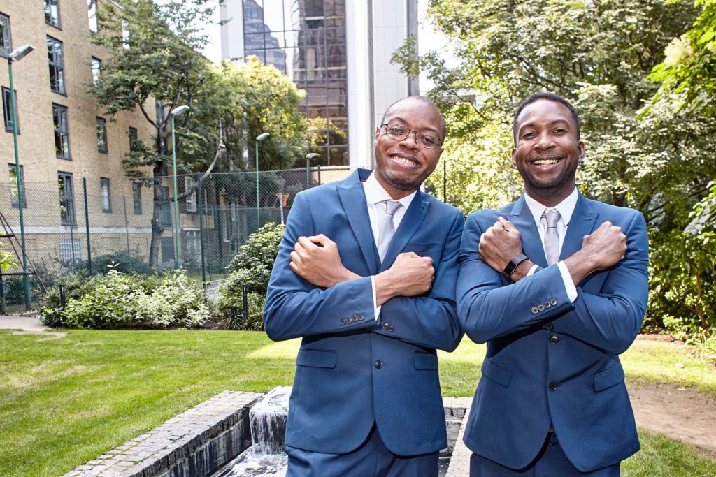 Groom and best man in blue suits posing with their arms crossed in a London garden