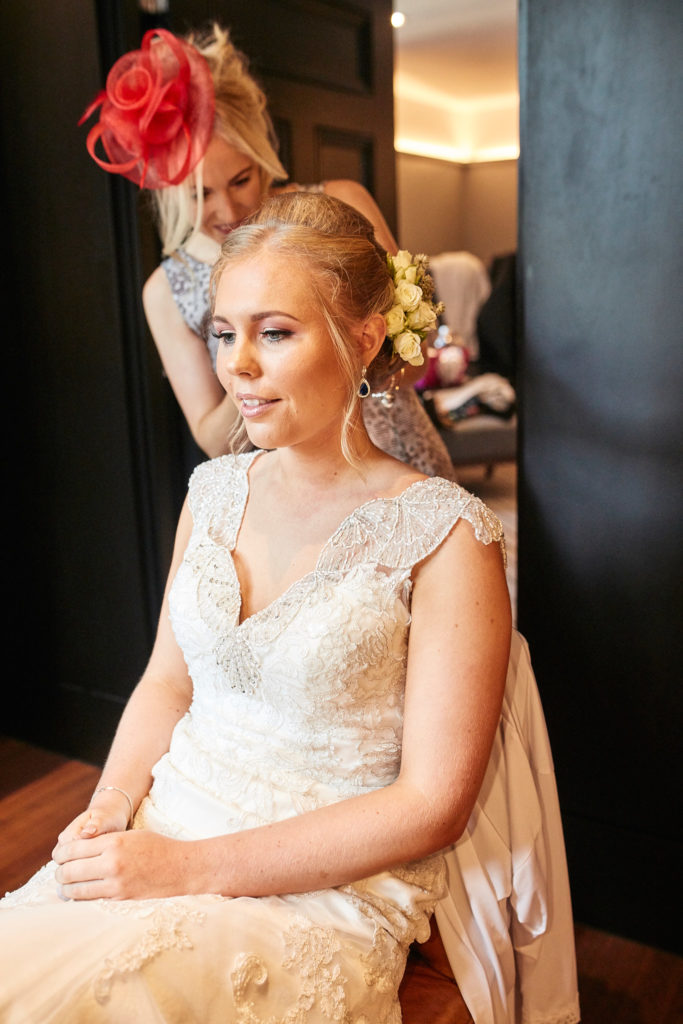 Bride sitting in her lace wedding dress as her veil is fitted