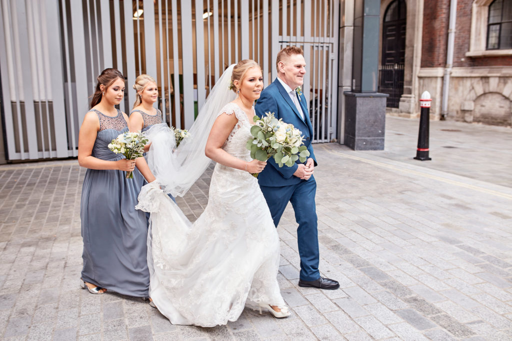 Bride walking to the church with her bridesmaids and a man in a blue suit