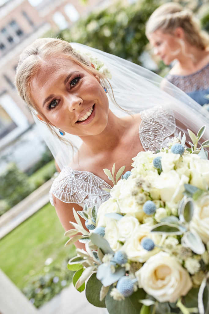 Bride smiling in her veil with her bouquet of white roses
