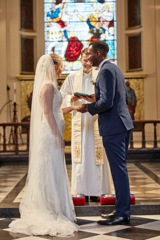Bride and groom exchanging vows in front of a stained glass window