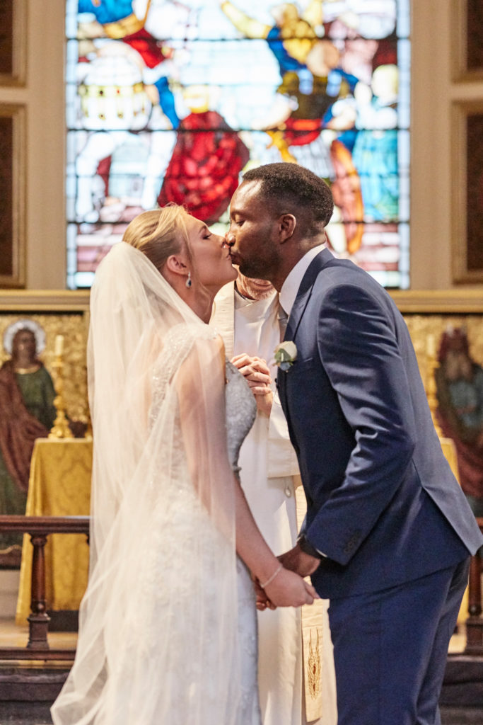 Bride and groom's first kiss in front of a stained glass window