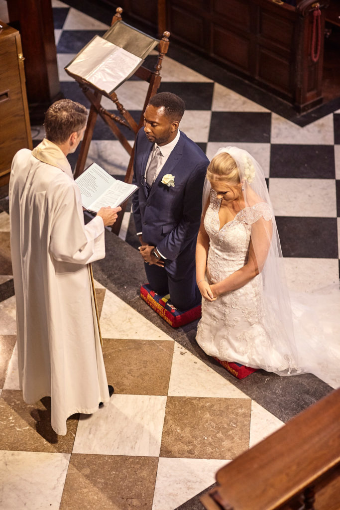 Bride and groom kneeling on the chequered church floor during the blessing