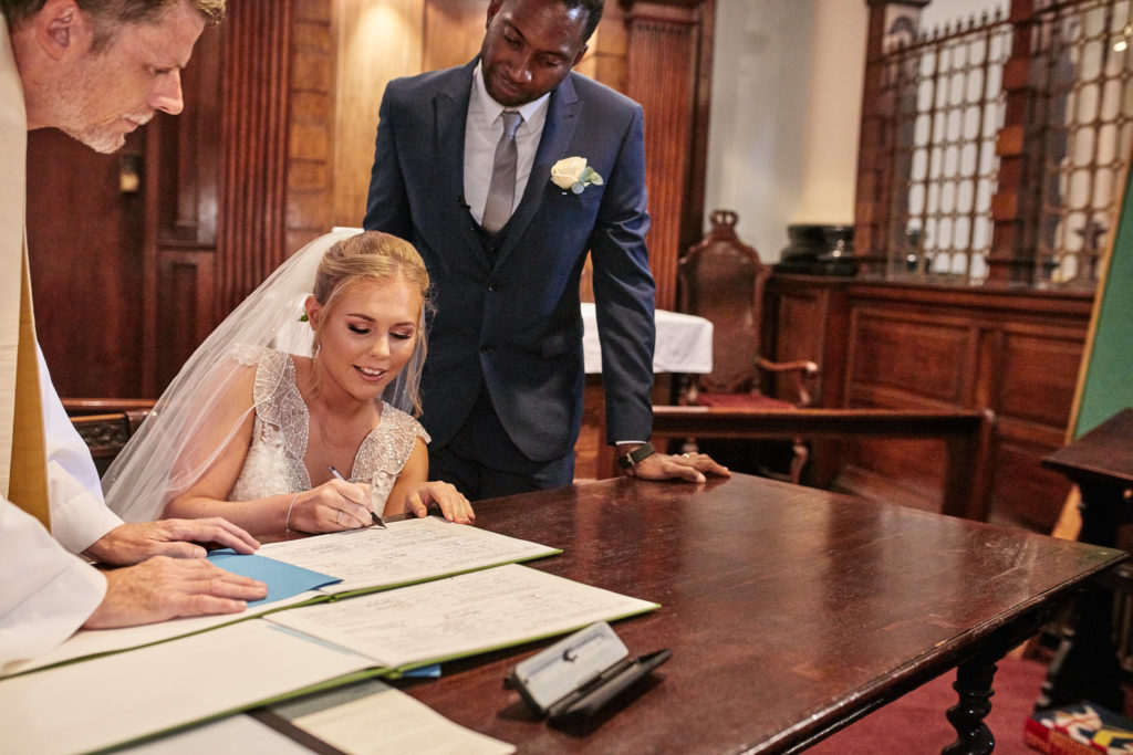 Bride signing the register as the groom looks on