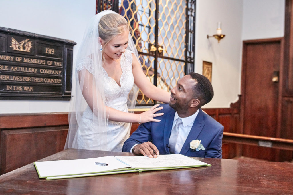 Bride standing beside the groom as he signs the register