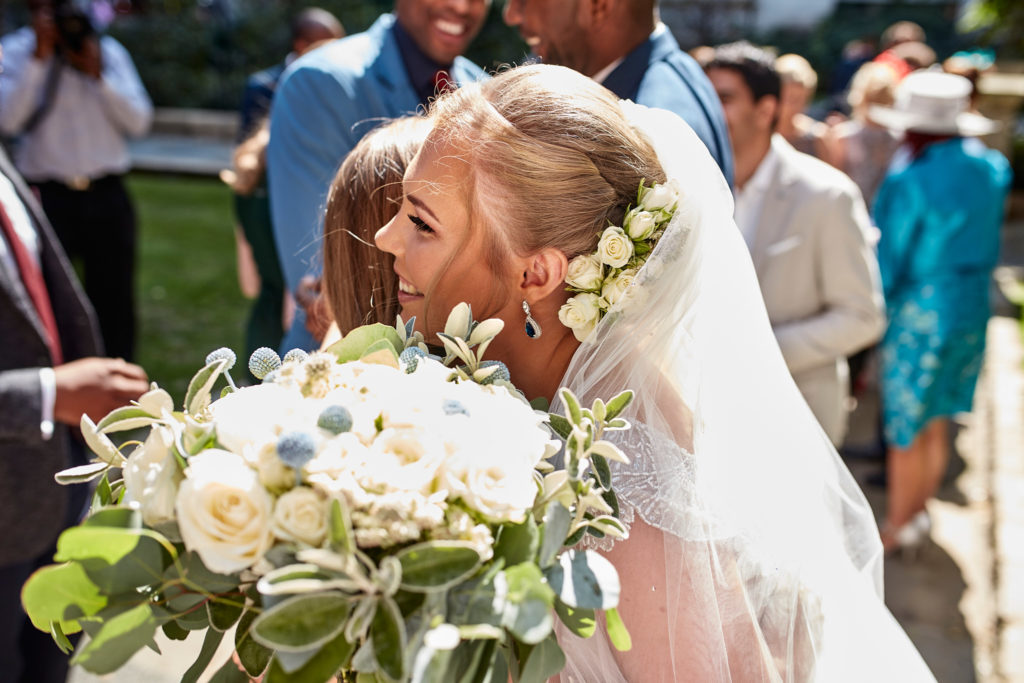 Bride smiling with her bouquet as guests gather after the ceremony
