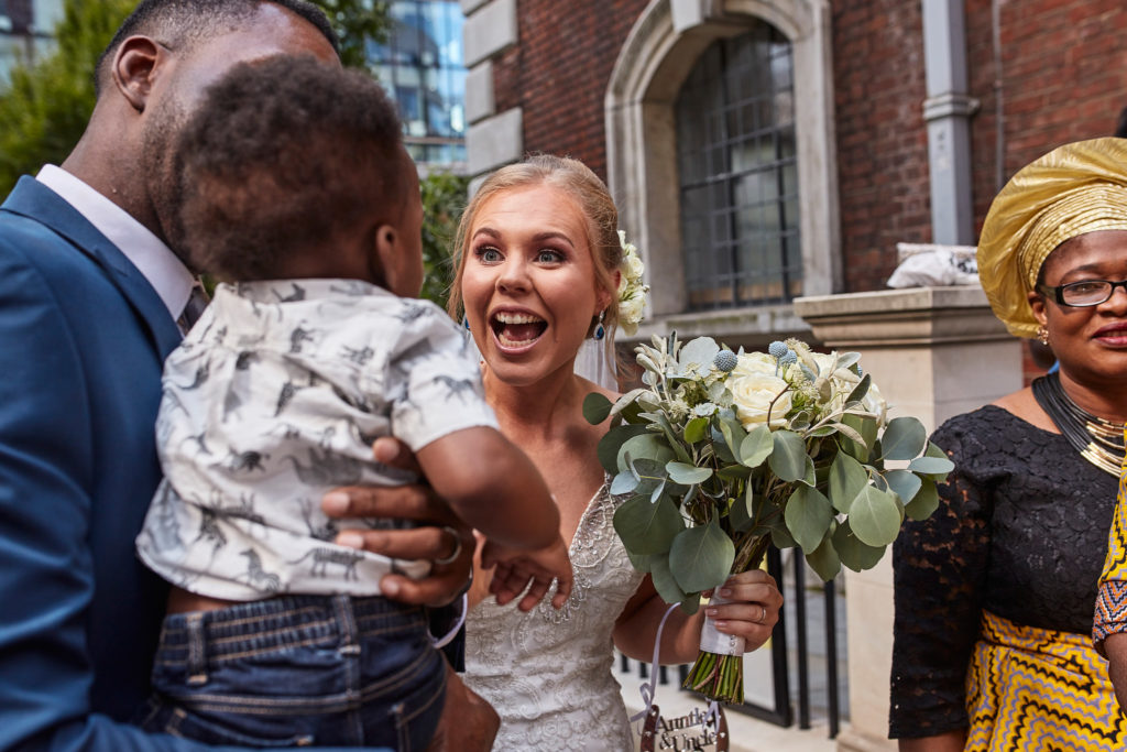 Bride laughing as the groom holds a baby outside the church