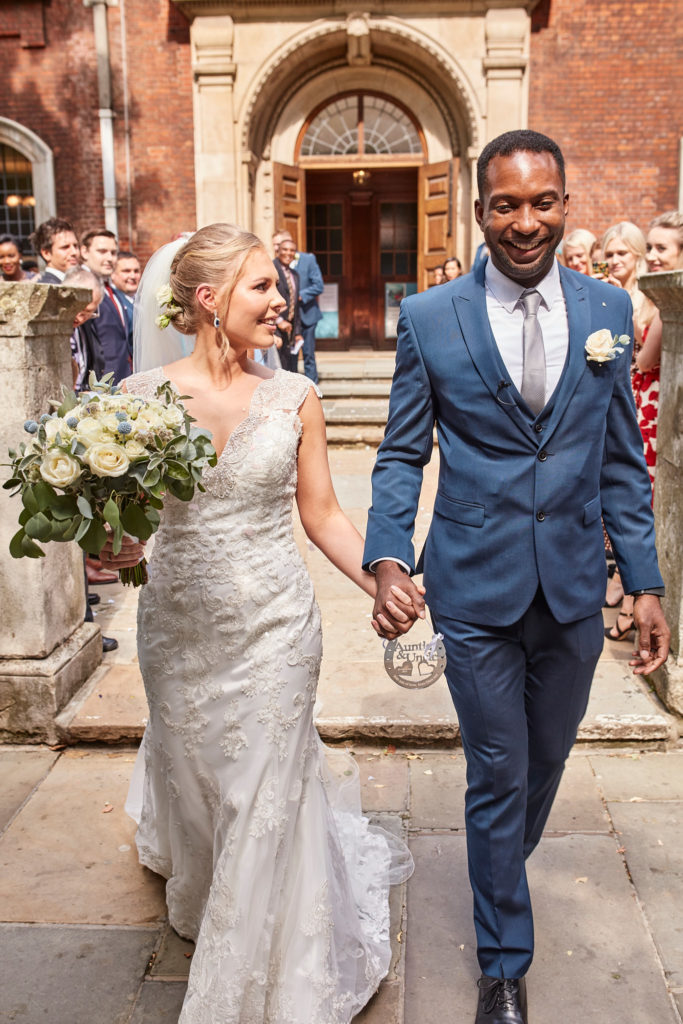 Bride and groom walking hand in hand from the church as guests look on