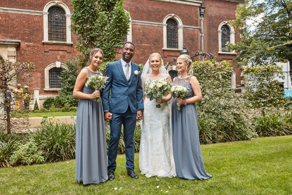 Bride and groom with two bridesmaids in grey dresses in a London churchyard garden