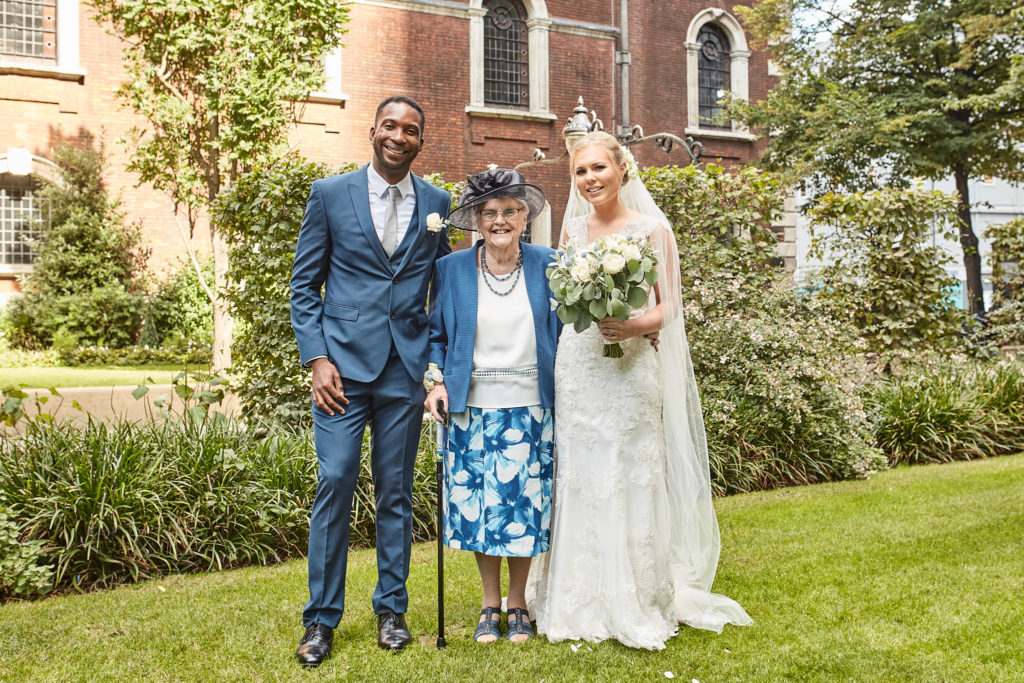 Bride and groom with an older guest in the churchyard garden