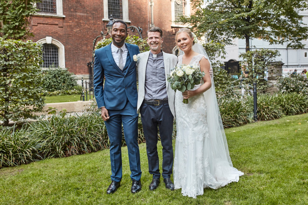 Bride and groom with a guest in the churchyard garden