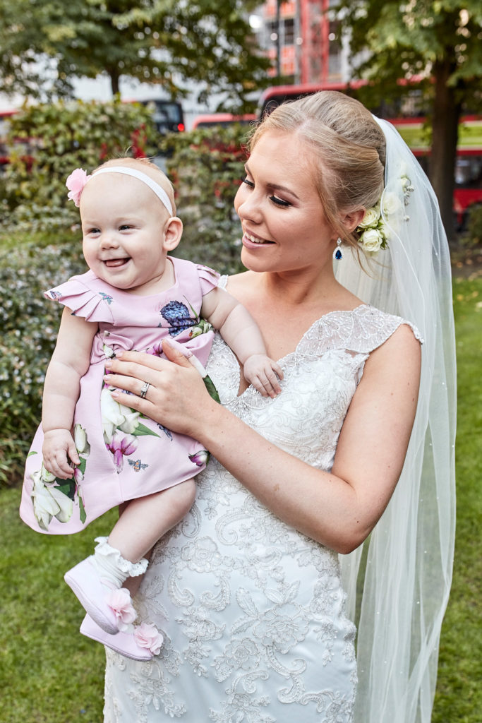 Bride holding a smiling baby in a pink dress
