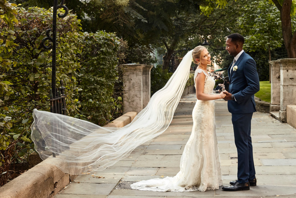 Bride and groom facing each other as her long veil streams out behind her