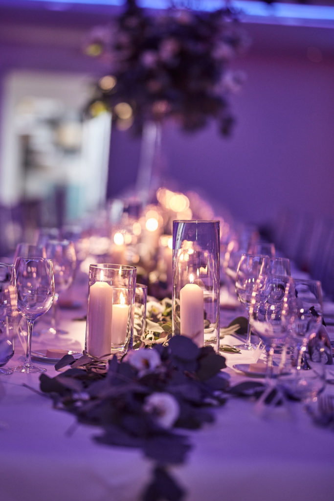 Candlelit wedding table with flowers and glassware under purple lighting at the Andaz