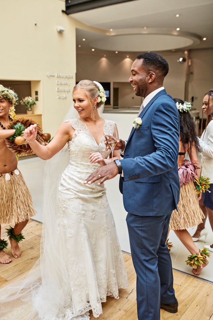 Bride and groom laughing as Polynesian dancers perform around them