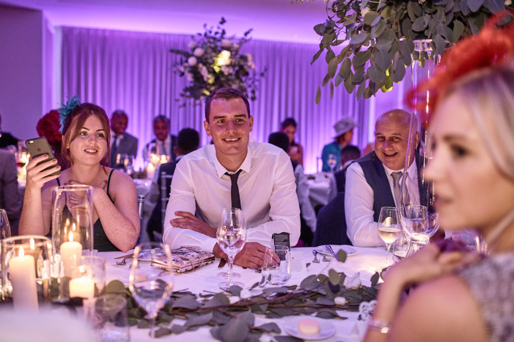 Wedding guests at a candlelit table under purple lights