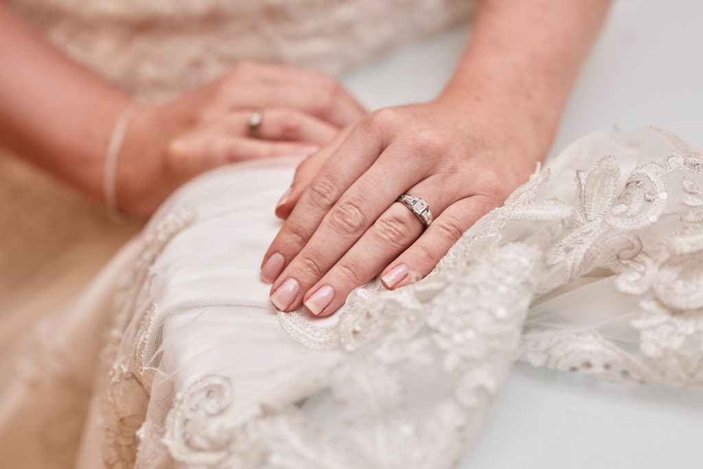 Close-up of the bride's hands and wedding ring resting on her lace dress