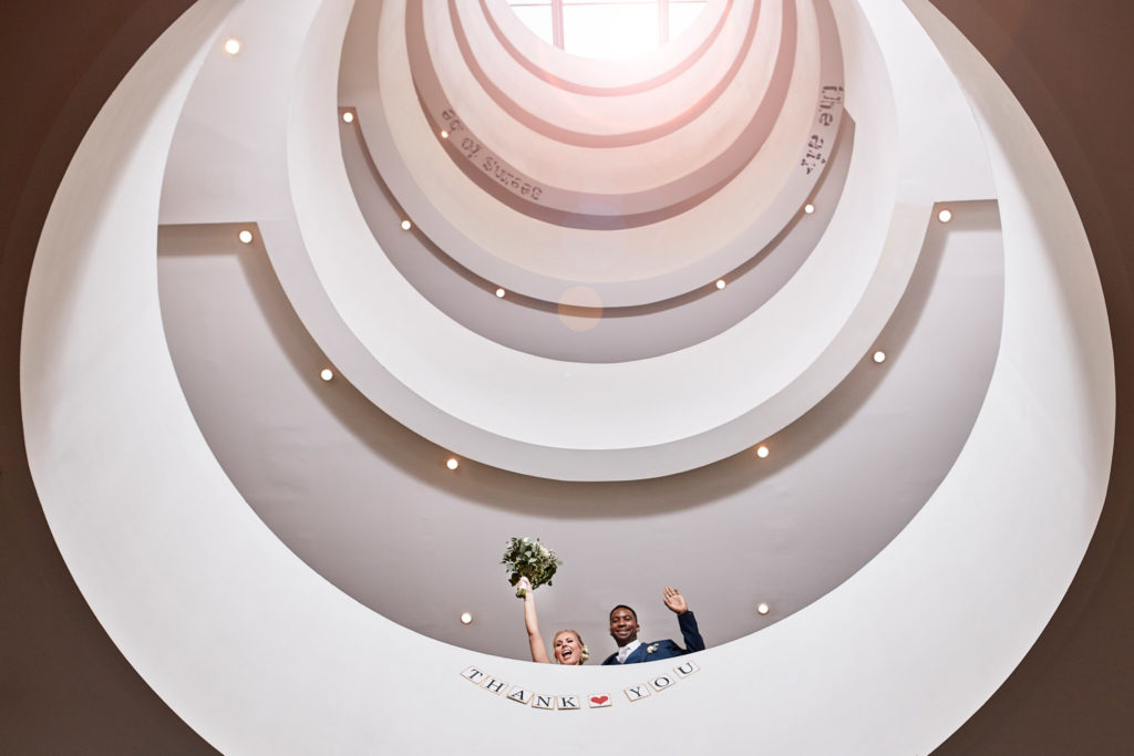 Bride and groom seen from below, leaning over a white spiral staircase at the Andaz