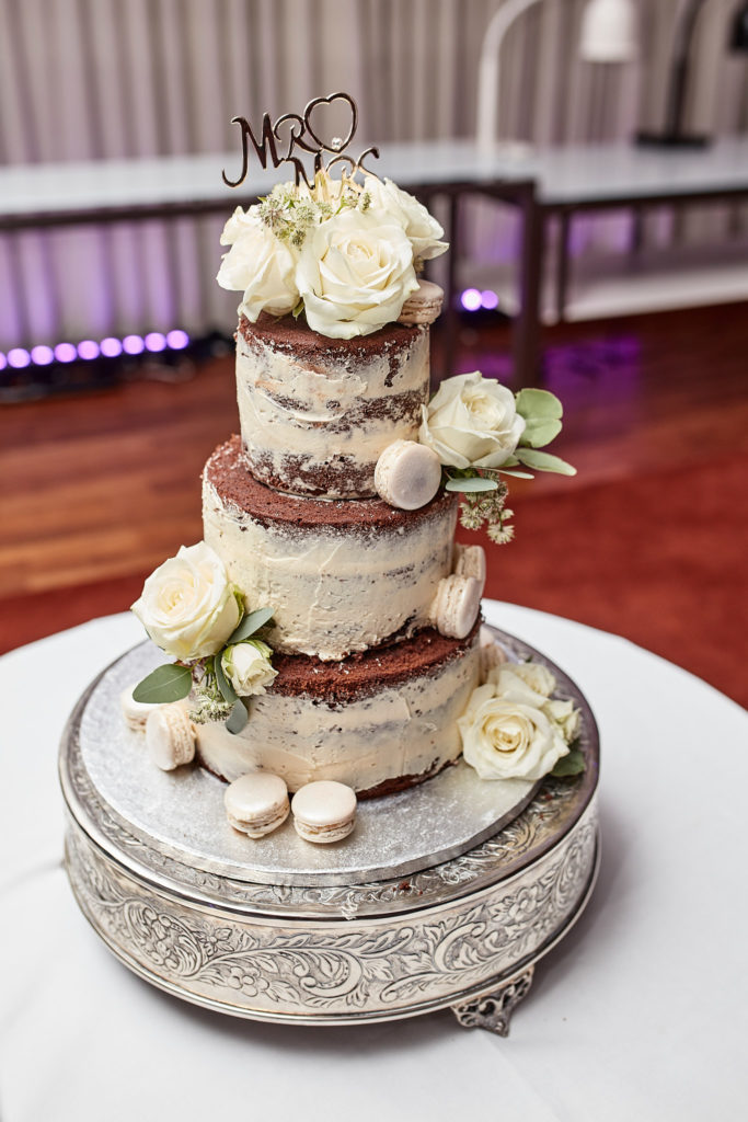 Three-tier naked wedding cake decorated with white roses and macarons