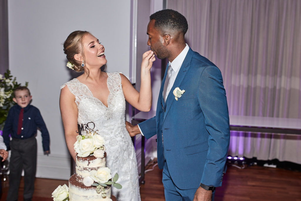 Bride laughing as she feeds the groom a piece of wedding cake
