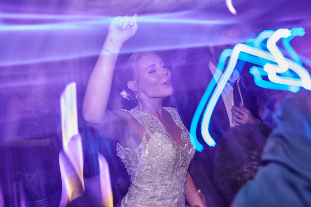 Bride dancing with her arm in the air among streaks of neon light