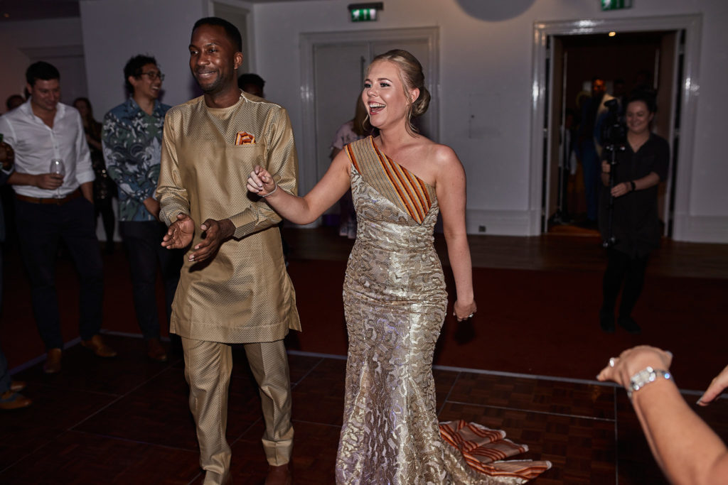 Bride in a gold sequinned dress dancing with the groom in a traditional outfit