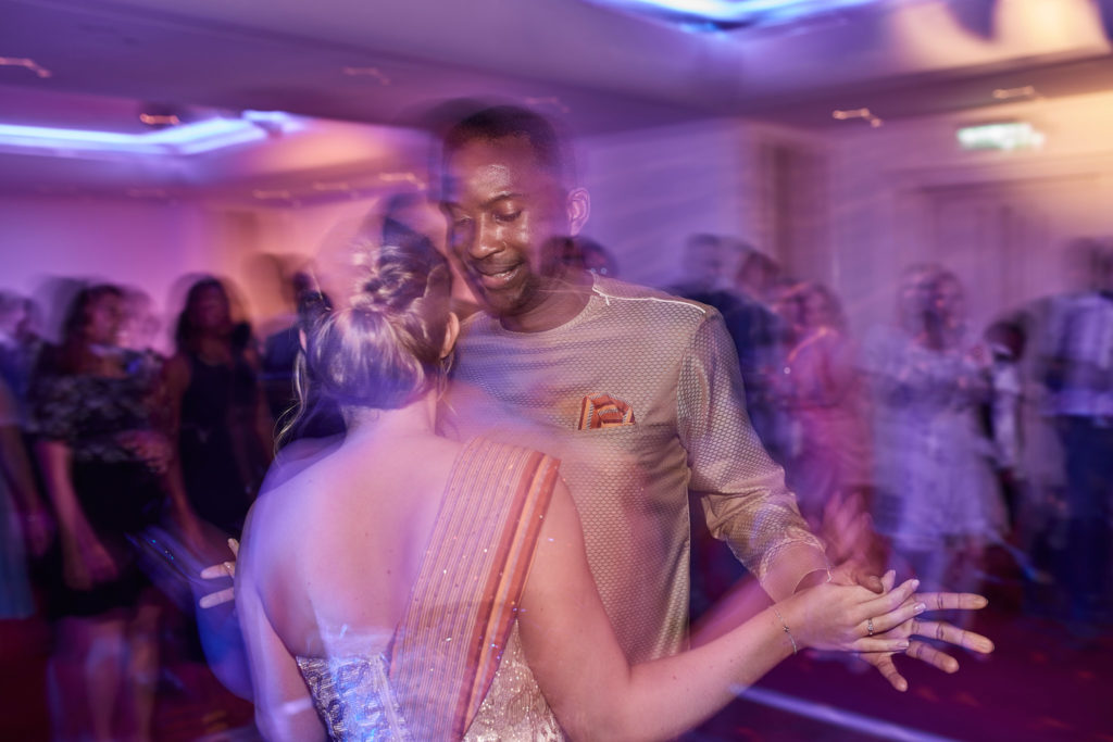 Bride and groom dancing among their guests under purple lights