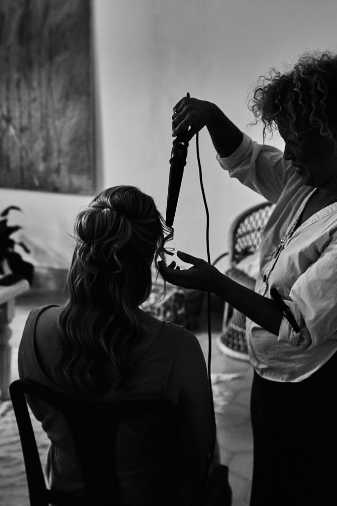 Black and white photo of a stylist curling a bridesmaid's hair
