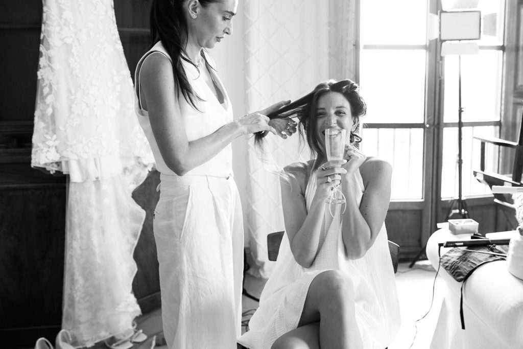 Black and white photo of the bride laughing as her hair is styled