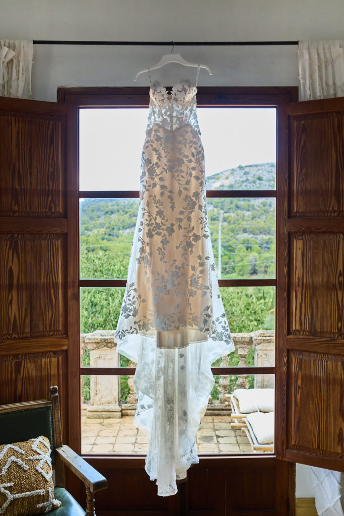 Lace wedding dress hanging in an open doorway overlooking the Mallorcan hills