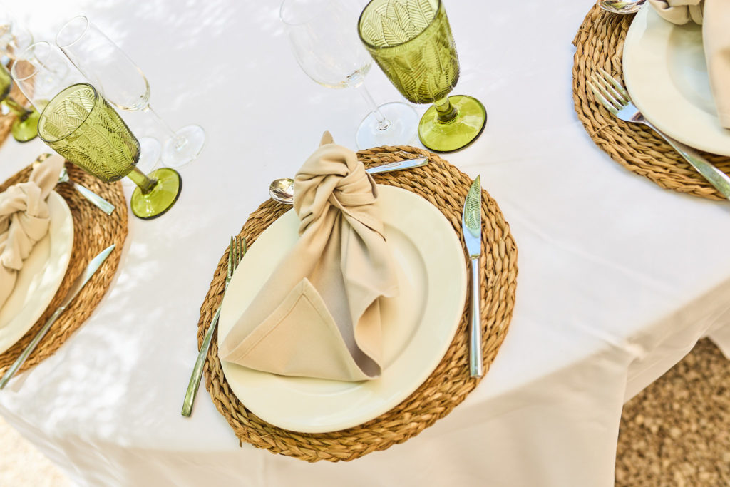 Table setting with woven placemats, bow-tied napkins and green glassware