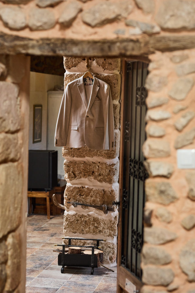 Groom's beige suit jacket hanging in a stone doorway