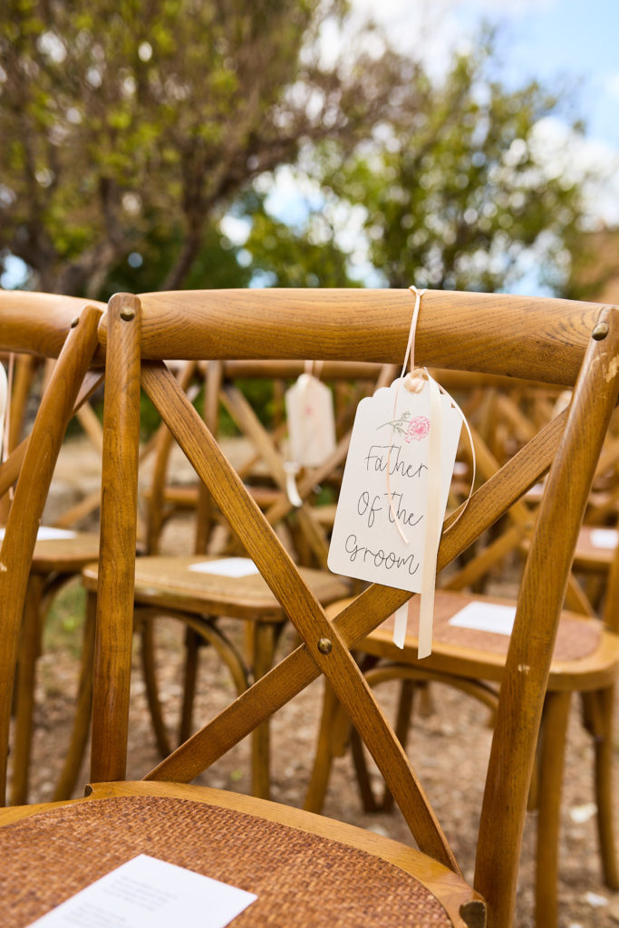 Wooden cross-back ceremony chairs with a luggage tag sign