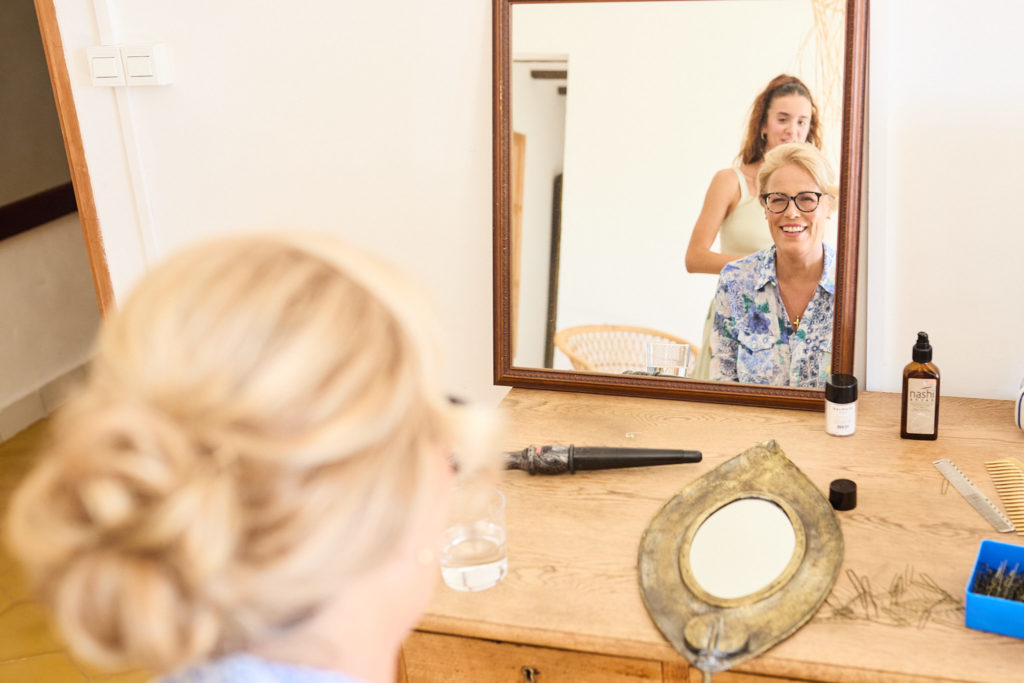 Bridesmaid with her hair up, seen from behind, with others reflected in a mirror