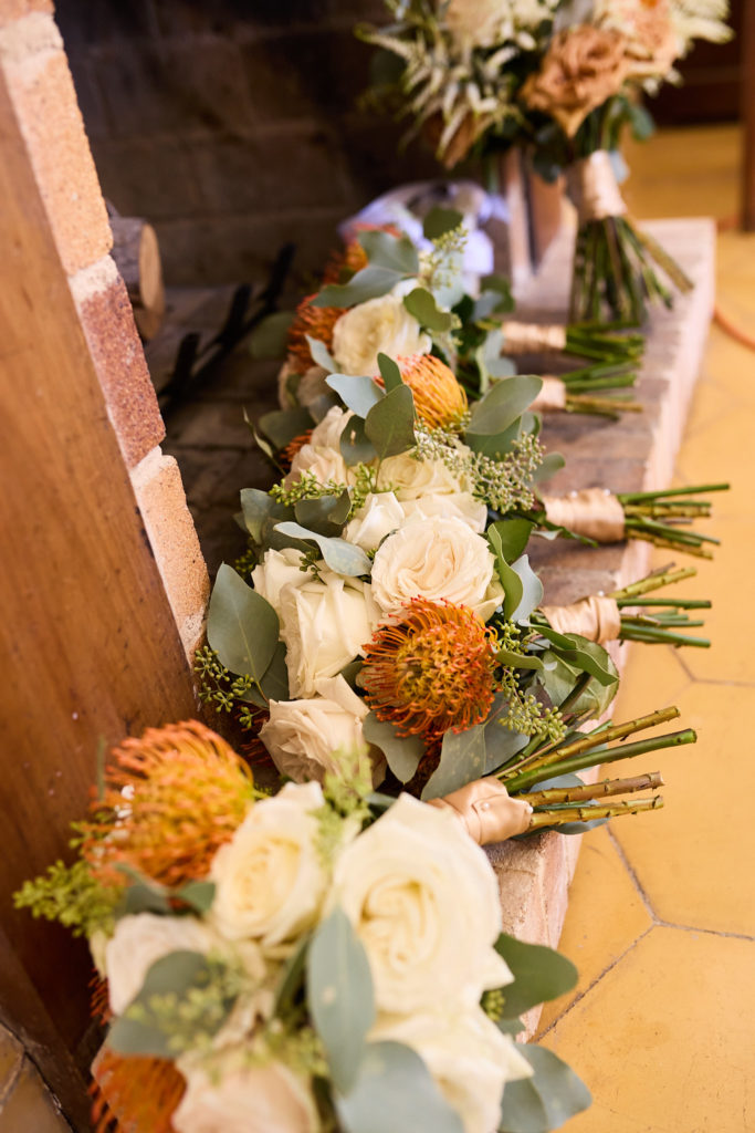 Row of bridesmaid bouquets of cream roses and orange proteas