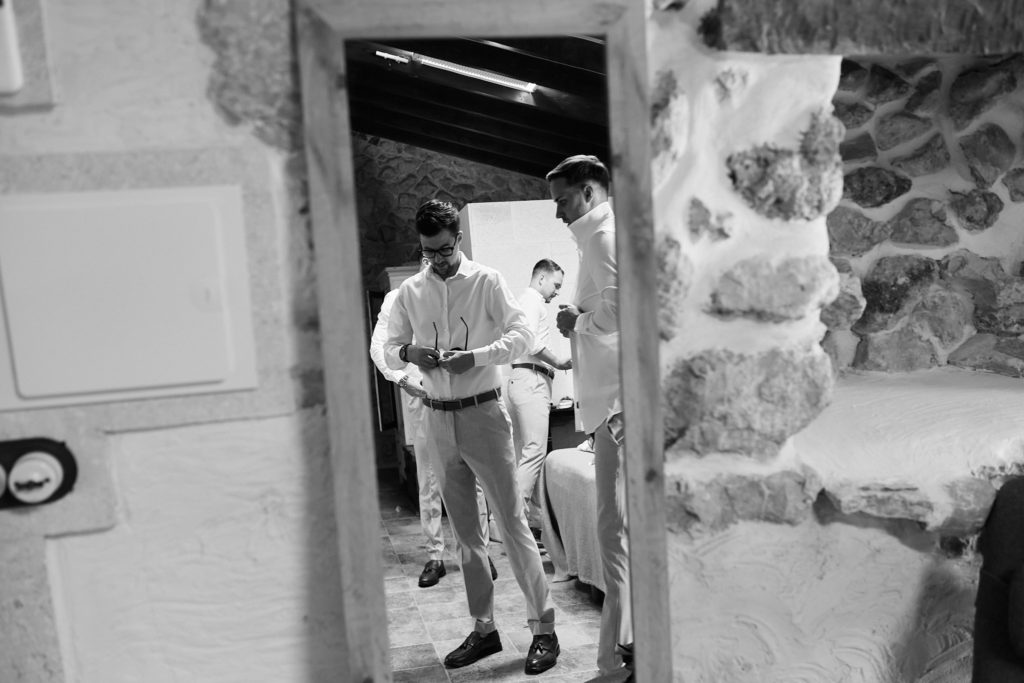 Black and white photo of the groomsmen getting ready, seen through a doorway
