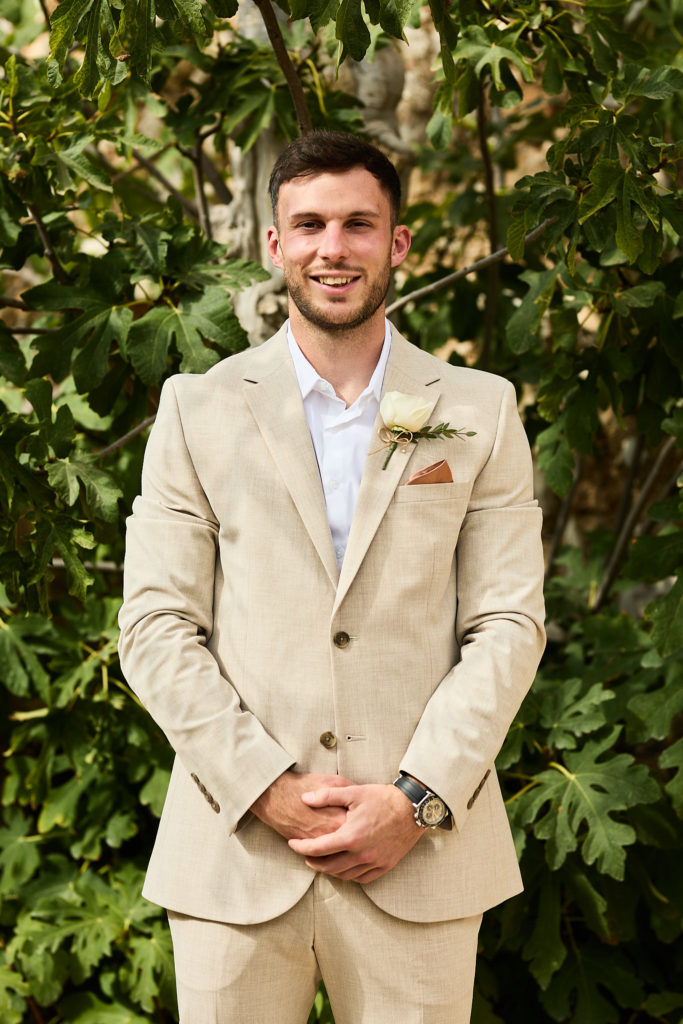 Groom smiling in a beige suit with a white buttonhole