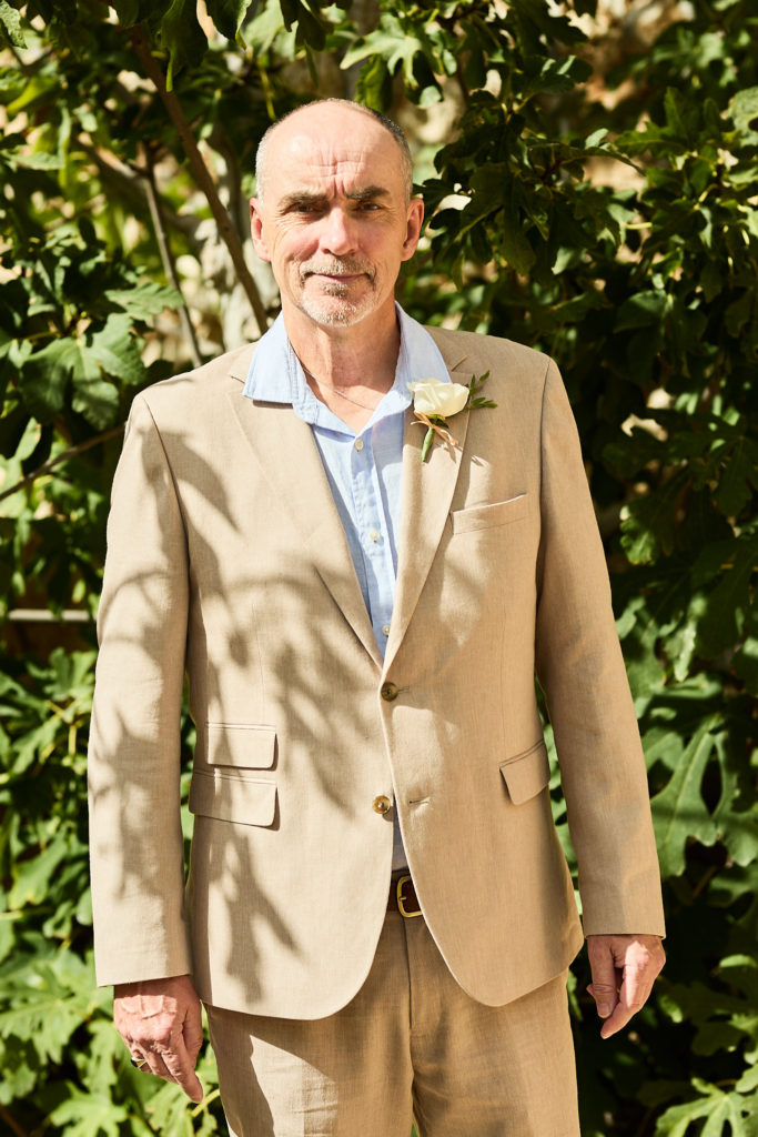 Older man in a beige suit and blue shirt with a white buttonhole