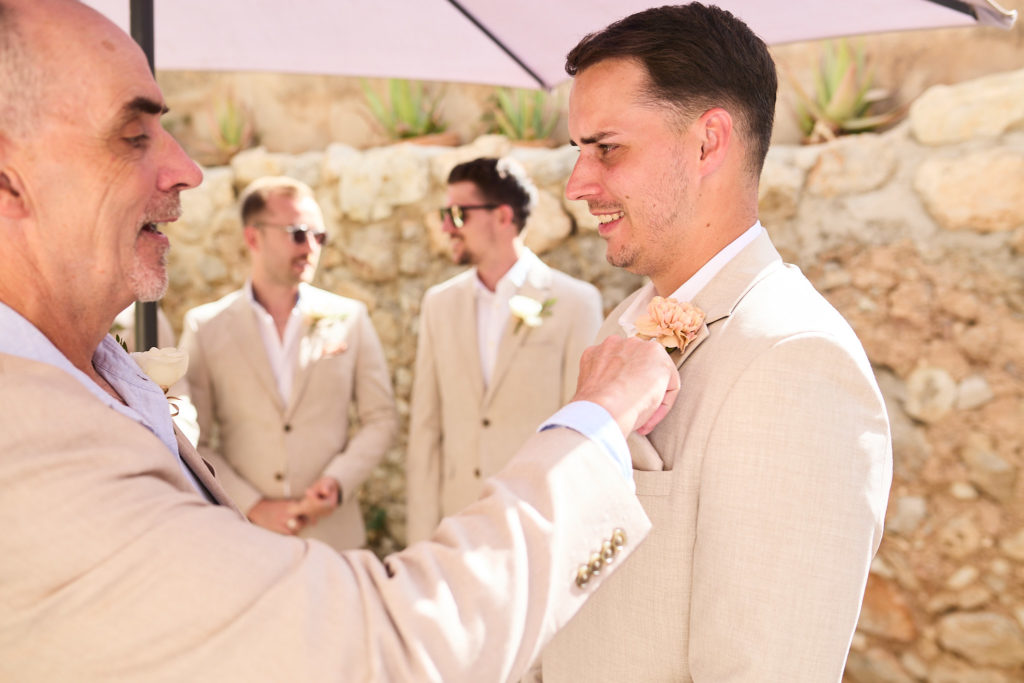 Older man pinning a buttonhole on the groom as groomsmen watch