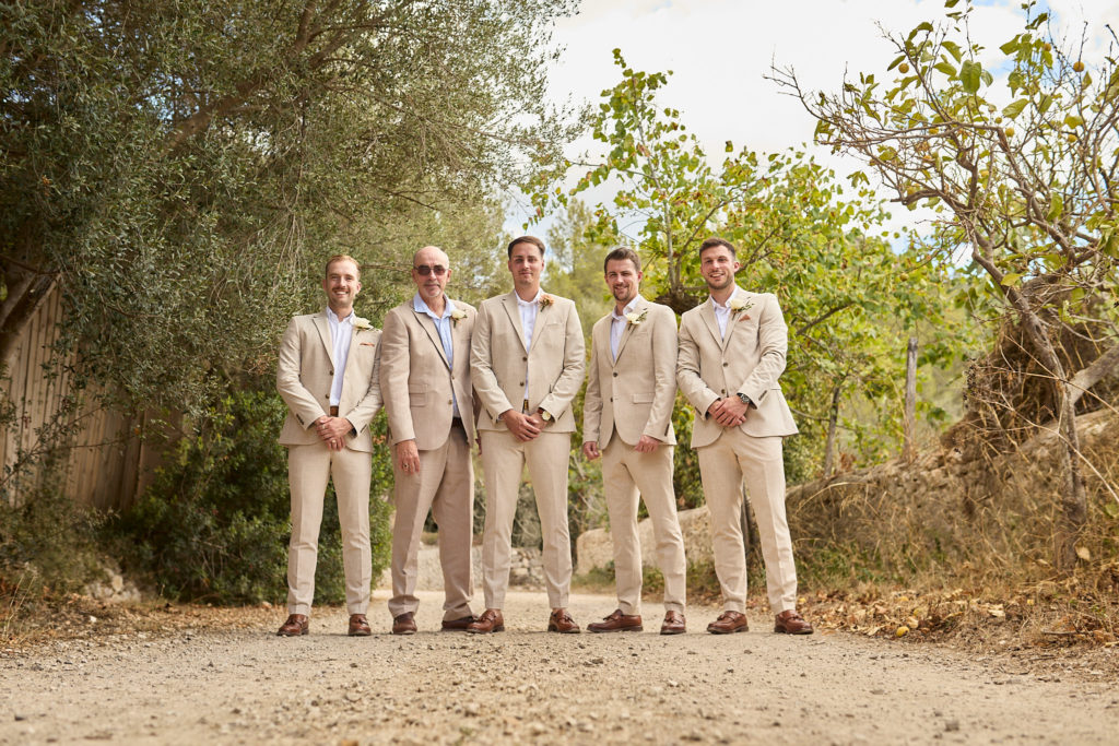 Groom and four groomsmen in beige suits standing among the trees at Son Boronat