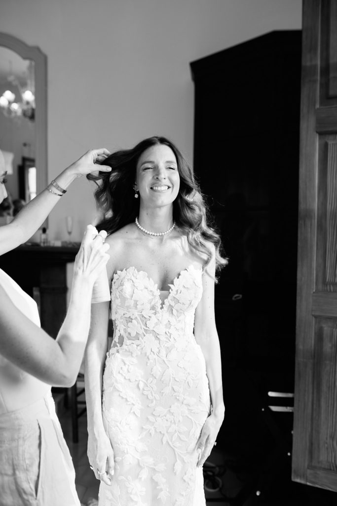 Black and white photo of the bride smiling in her lace wedding dress as her hair is adjusted