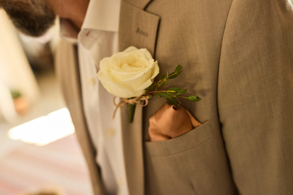 Close-up of a white rose buttonhole on a beige suit