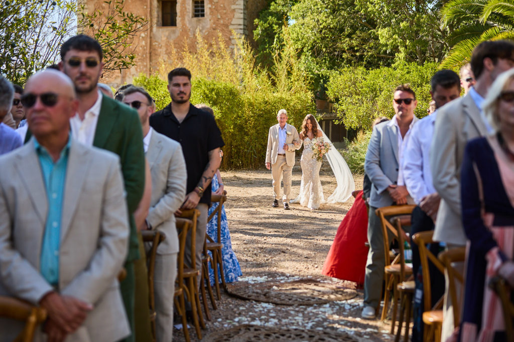 Wedding guests turning to watch the bride arrive at the outdoor ceremony