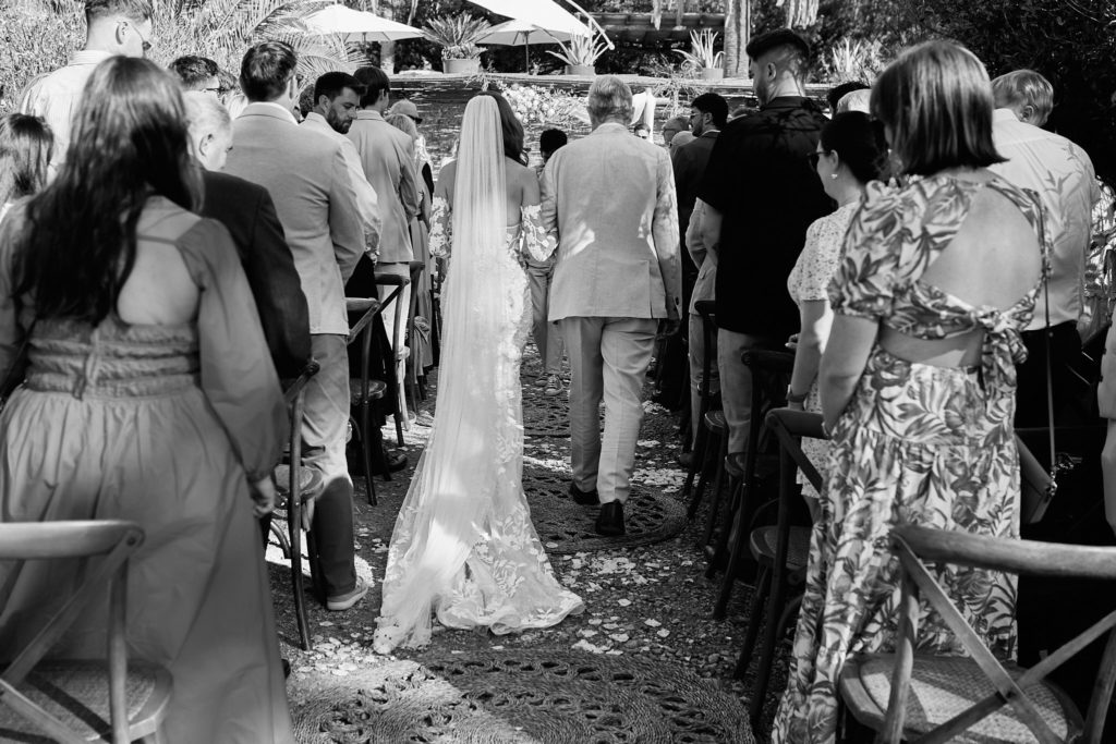Black and white photo of the bride walking down the aisle, seen from behind